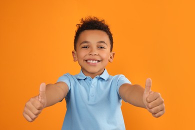 Photo of African-American boy showing thumbs up on orange background