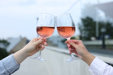 Photo of Women clinking glasses with rose wine outdoors, closeup