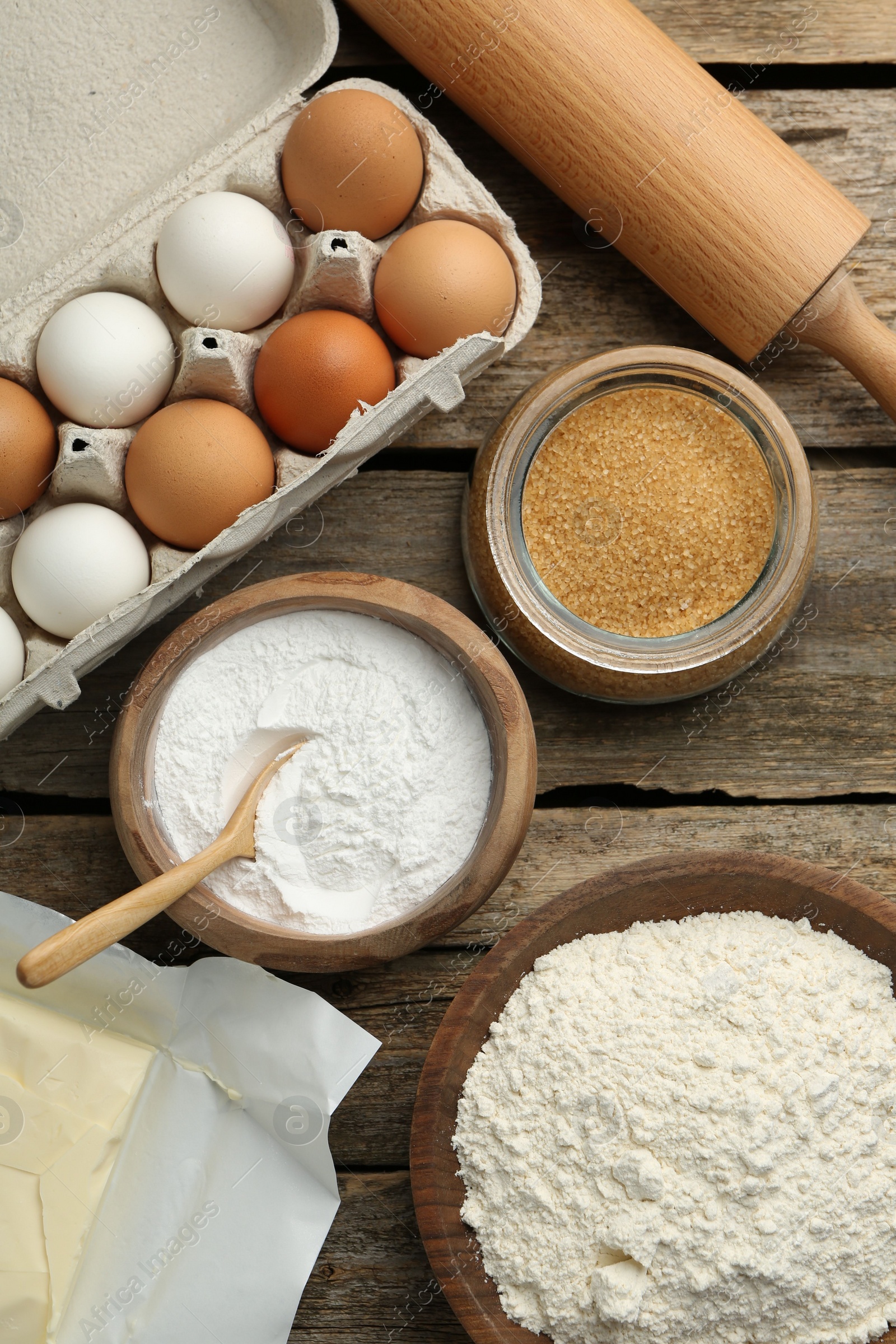 Photo of Ingredients for making dough and rolling pin on wooden table, flat lay