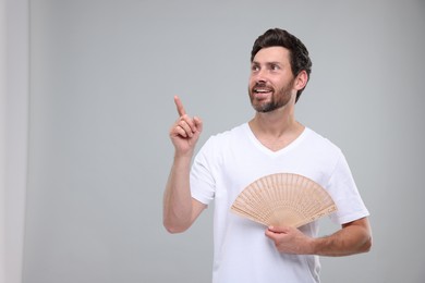 Photo of Happy man holding hand fan on light grey background. Space for text