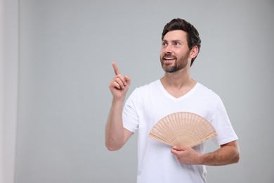 Happy man holding hand fan on light grey background. Space for text