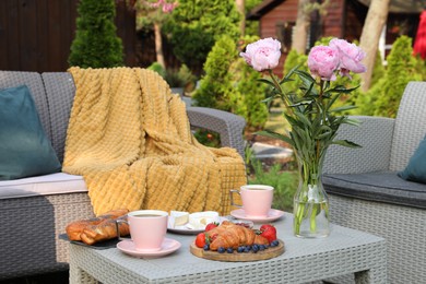 Photo of Morning drink, pastry, berries, cheese and vase with flowers on rattan table. Summer breakfast outdoors