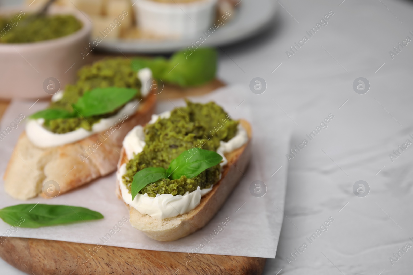 Photo of Tasty bruschettas with cream cheese, pesto sauce and fresh basil on white table, closeup. Space for text
