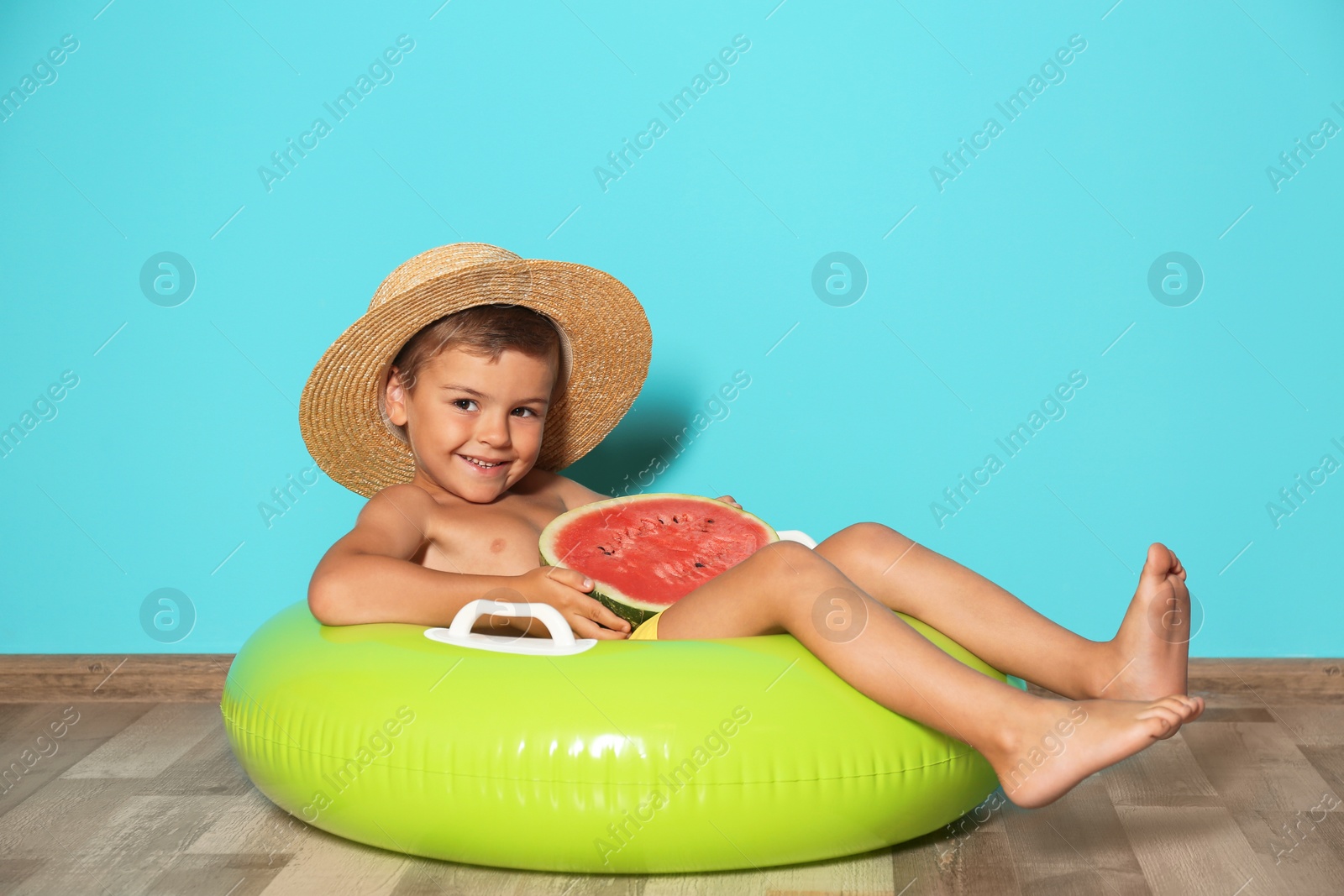 Photo of Cute little boy with inflatable ring and watermelon near color wall