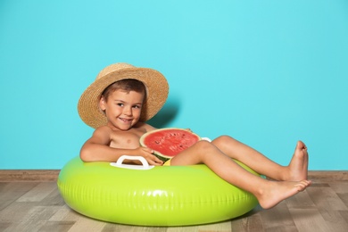 Photo of Cute little boy with inflatable ring and watermelon near color wall