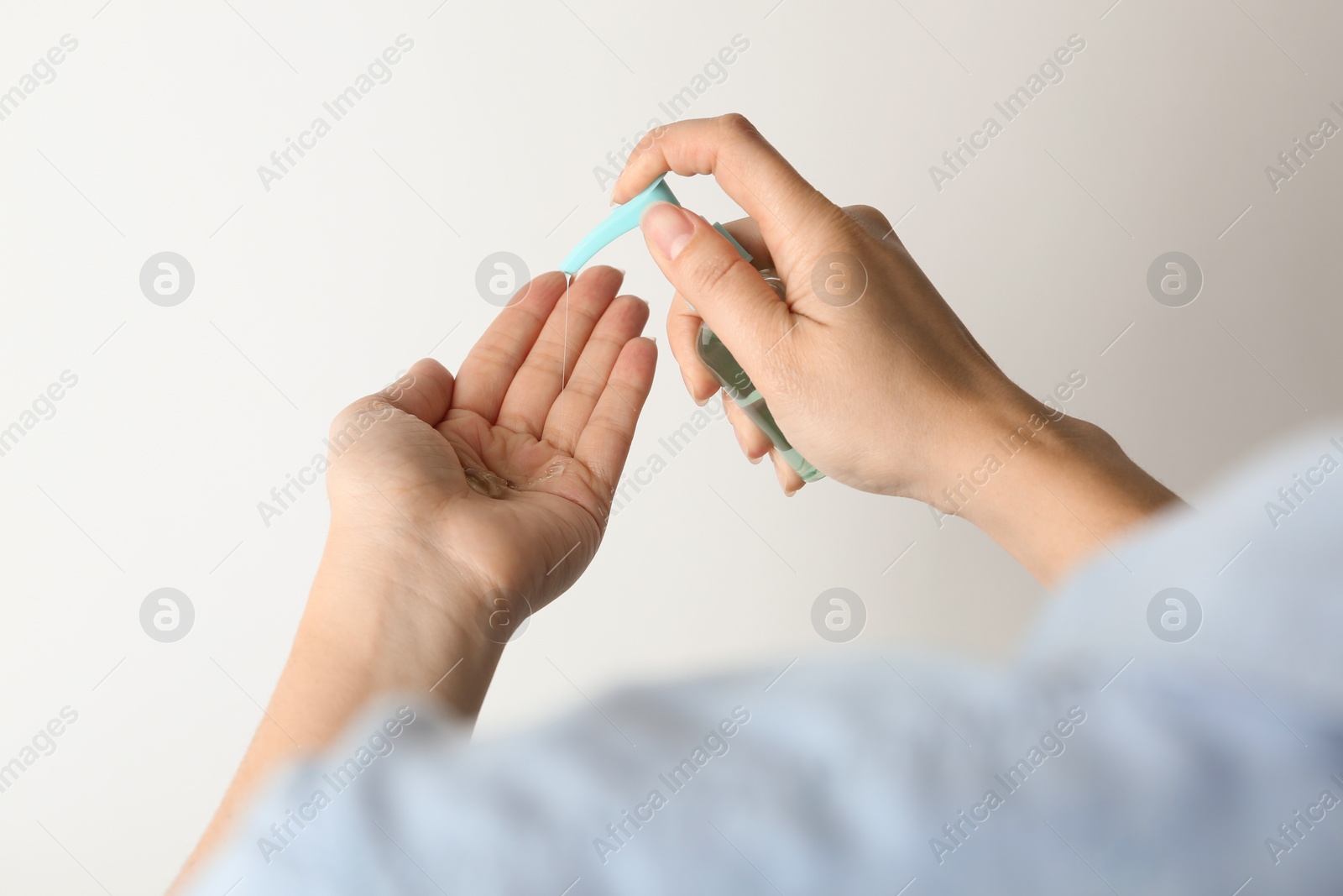 Photo of Woman applying antiseptic gel onto hand against light background, closeup. Virus prevention