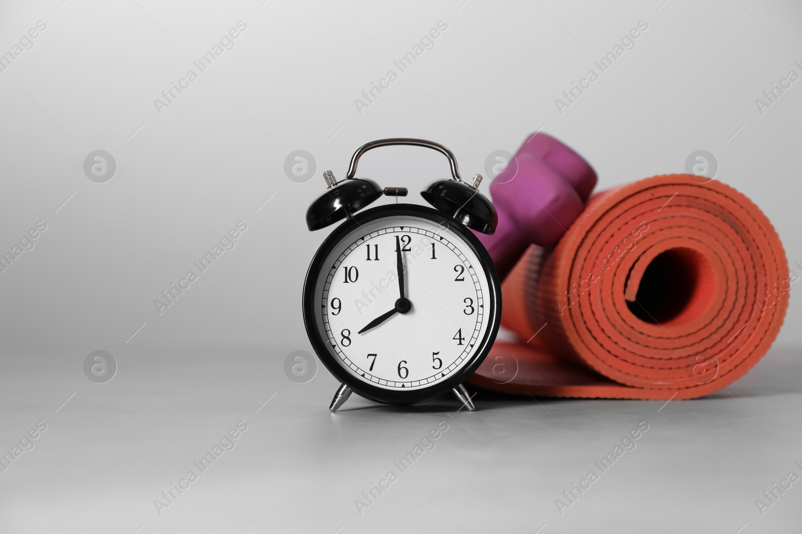 Photo of Alarm clock, yoga mat and dumbbells on grey background, space for text. Morning exercise