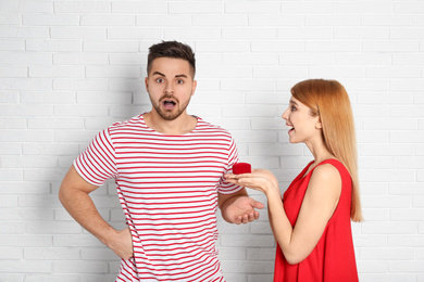 Young woman with engagement ring making marriage proposal to her boyfriend near white brick wall