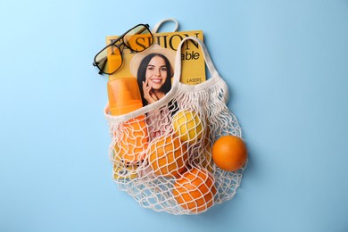 Photo of String bag with magazine, fruits and summer accessories on light blue background, flat lay