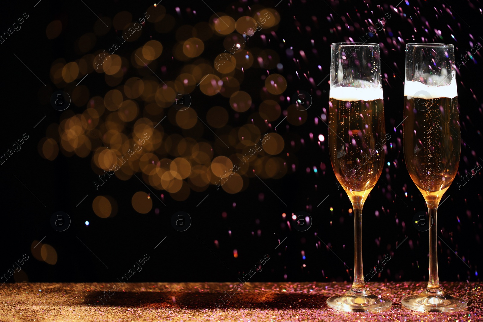 Photo of Glasses of champagne and golden glitter on table against blurred background. Space for text