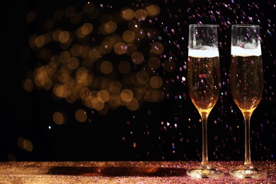 Photo of Glasses of champagne and golden glitter on table against blurred background. Space for text