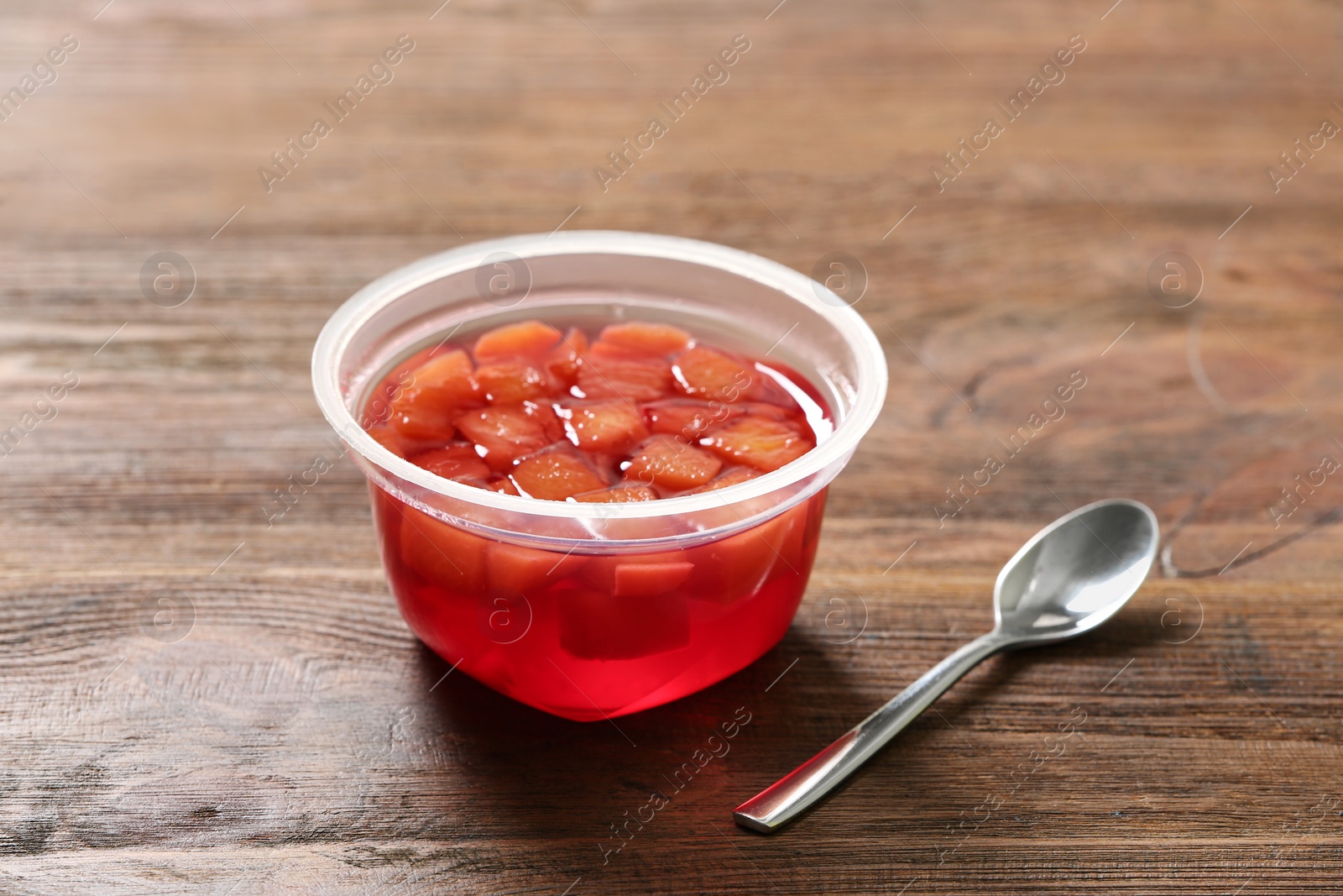 Photo of Plastic container with tasty jelly and spoon on wooden table