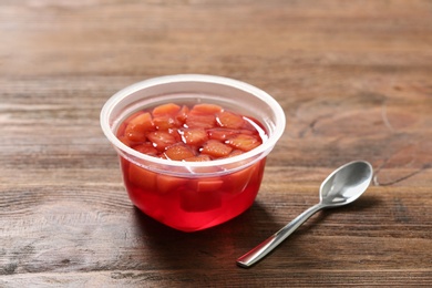 Photo of Plastic container with tasty jelly and spoon on wooden table