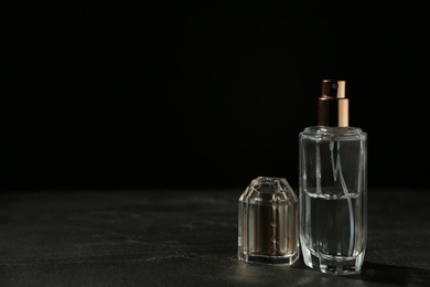 Photo of Bottle of perfume on dark table against black background, space for text
