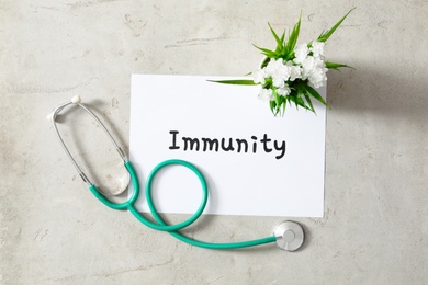 Photo of Sheet of paper with word Immunity, stethoscope and flowers on light background, flat lay