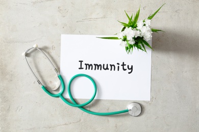 Sheet of paper with word Immunity, stethoscope and flowers on light background, flat lay