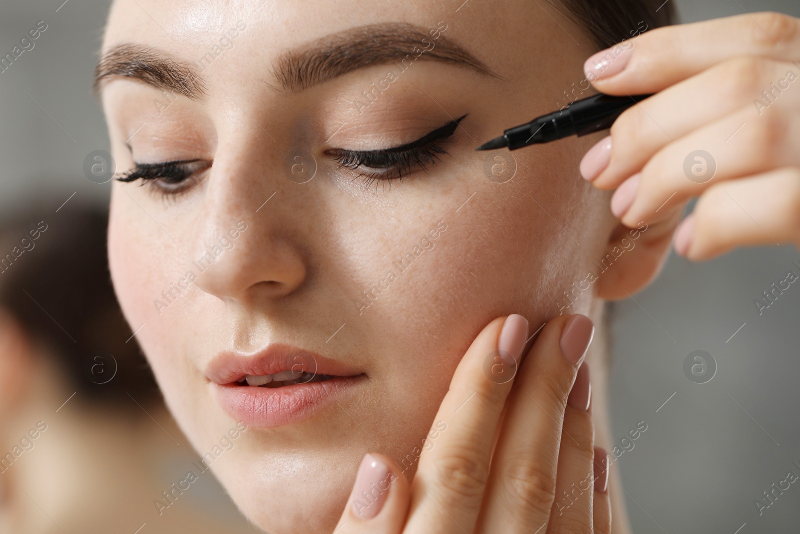 Photo of Makeup product. Woman applying black eyeliner on blurred background, closeup