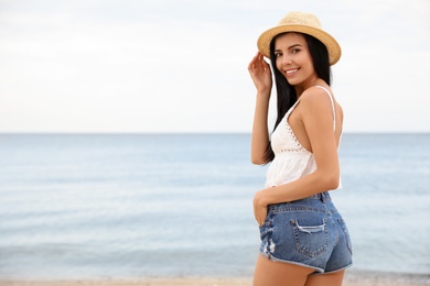 Photo of Beautiful young woman with beach hat near sea. Space for text