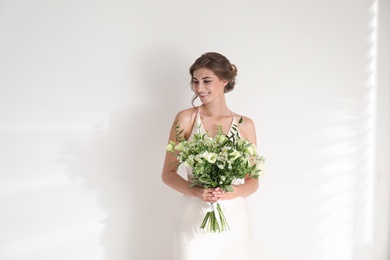 Young bride wearing wedding dress with beautiful bouquet on light background