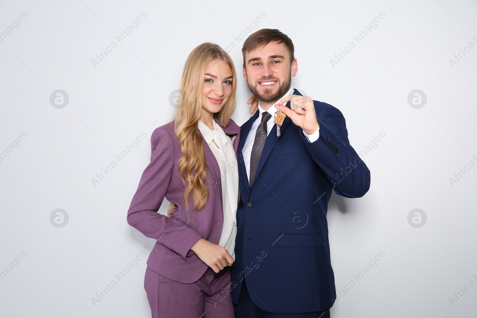 Photo of Happy young business people with house key on light background