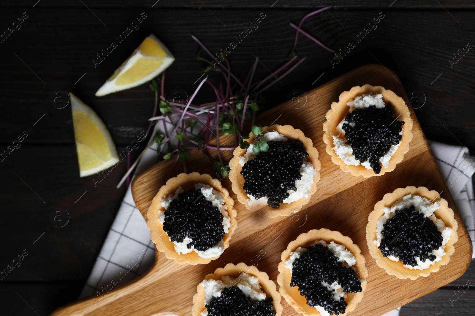 Photo of Board of delicious tartlets with black caviar and cream cheese on wooden table, top view