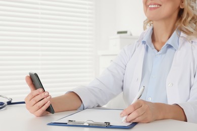 Photo of Doctor with smartphone and clipboard at desk in clinic, closeup. Online medicine concept
