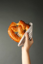 Woman with tasty freshly baked pretzel on grey background, closeup