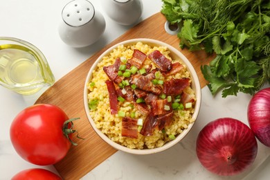 Tasty millet porridge with bacon and green onion in bowl on white marble table, flat lay