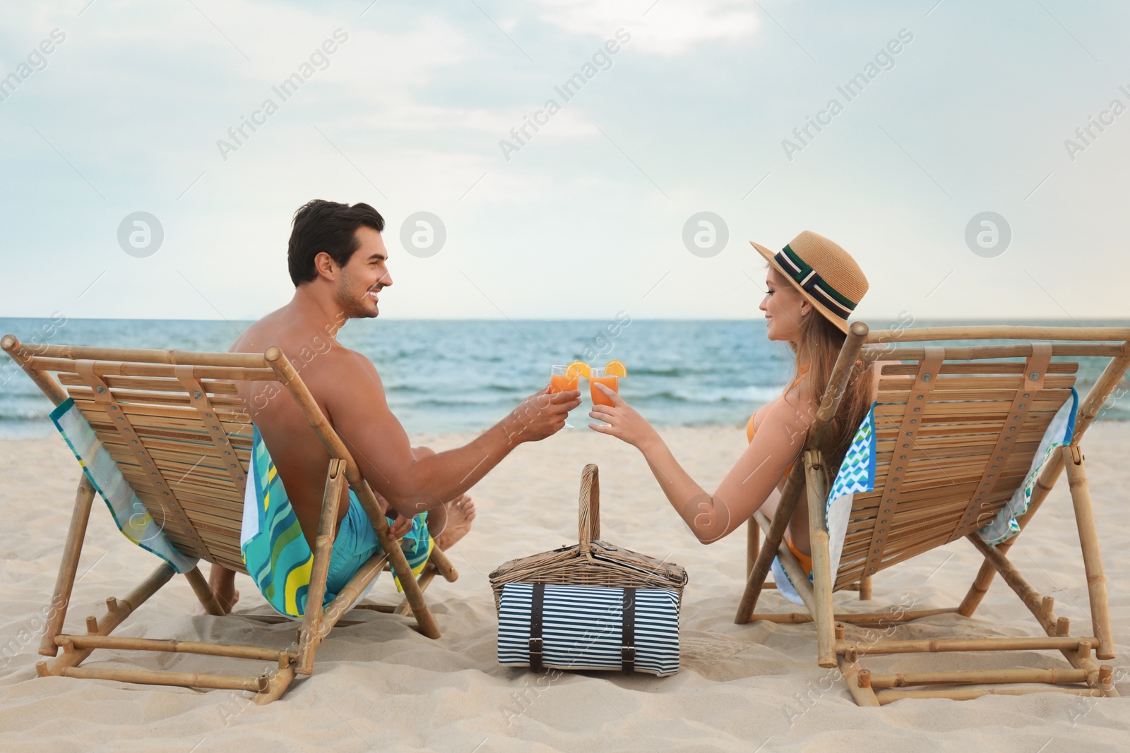 Photo of Happy young couple with cocktails sitting on deck chairs at sea beach