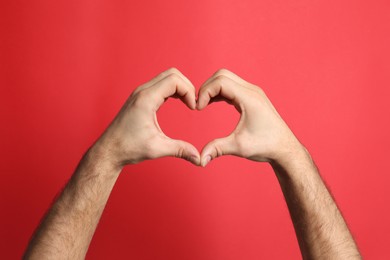 Photo of Man making heart with his hands on red background, closeup