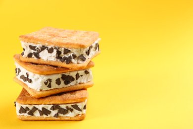 Photo of Sweet delicious ice cream cookie sandwiches on yellow background, closeup. Space for text