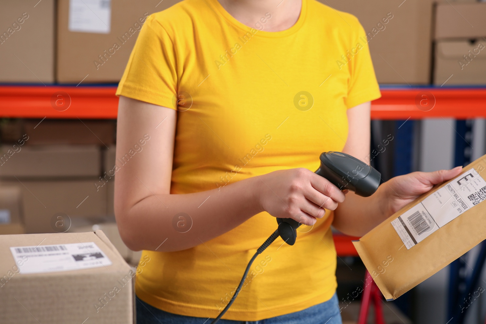 Photo of Post office worker with scanner reading parcel barcode indoors, closeup