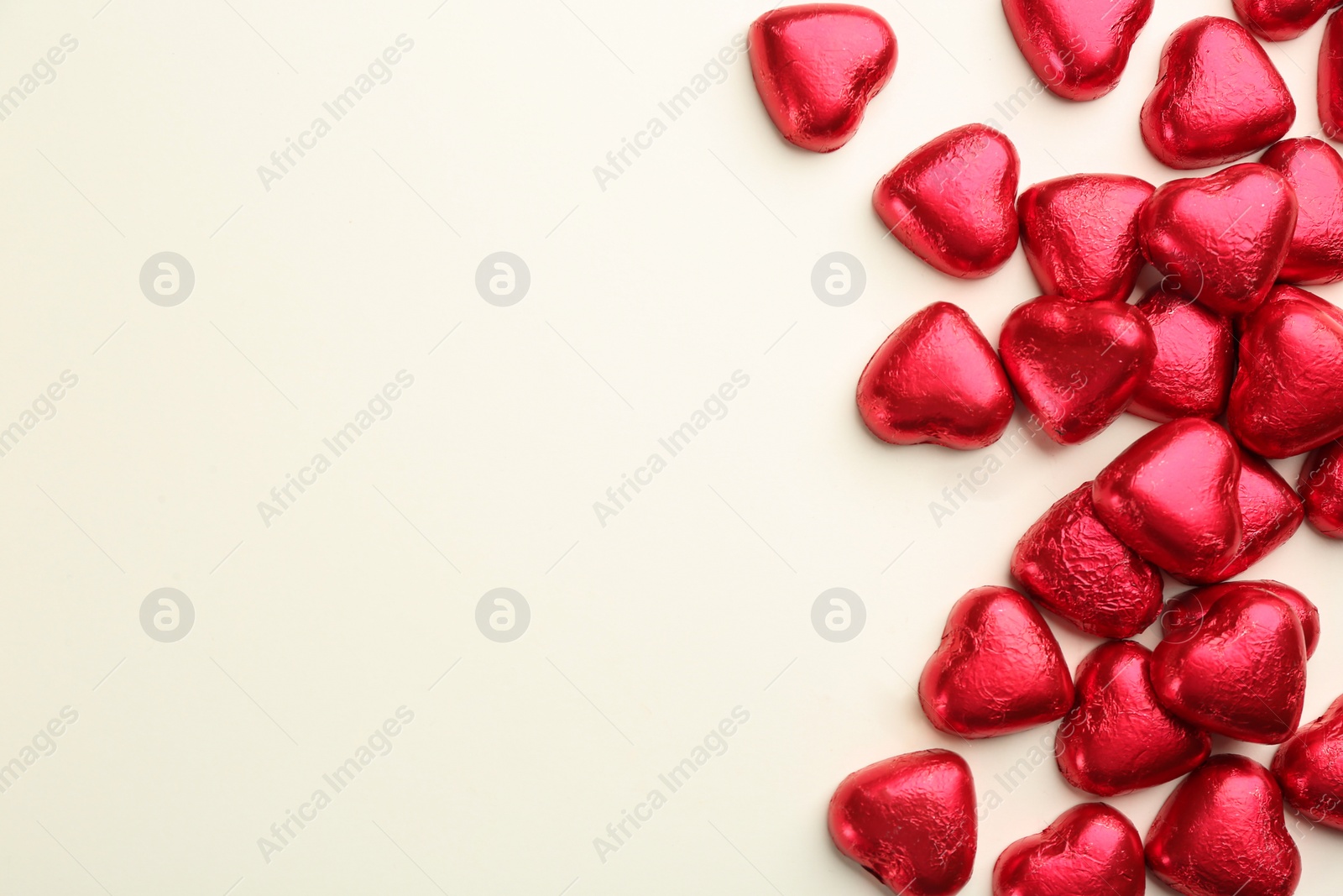 Photo of Heart shaped chocolate candies in red foil on beige background, flat lay. Space for text