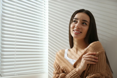 Young woman near window with Venetian blinds. Space for text