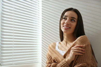 Photo of Young woman near window with Venetian blinds. Space for text