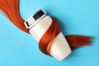 Photo of Bottle wrapped in lock of hair on light blue background, top view. Natural cosmetic product