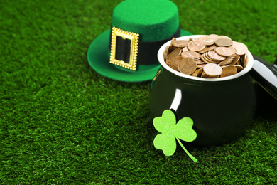 Photo of Pot of gold coins, hat and clover on green grass, space for text. St. Patrick's Day celebration