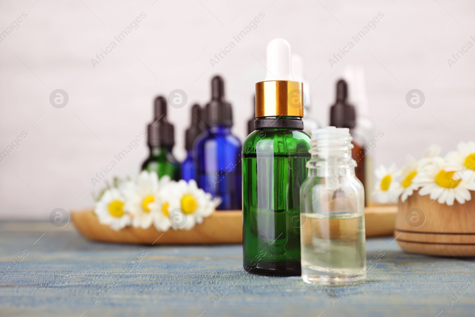 Photo of Bottles of chamomile essential oil and flowers on color table, space for text