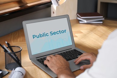Image of Public Sector. Man working with modern laptop at wooden table, closeup 
