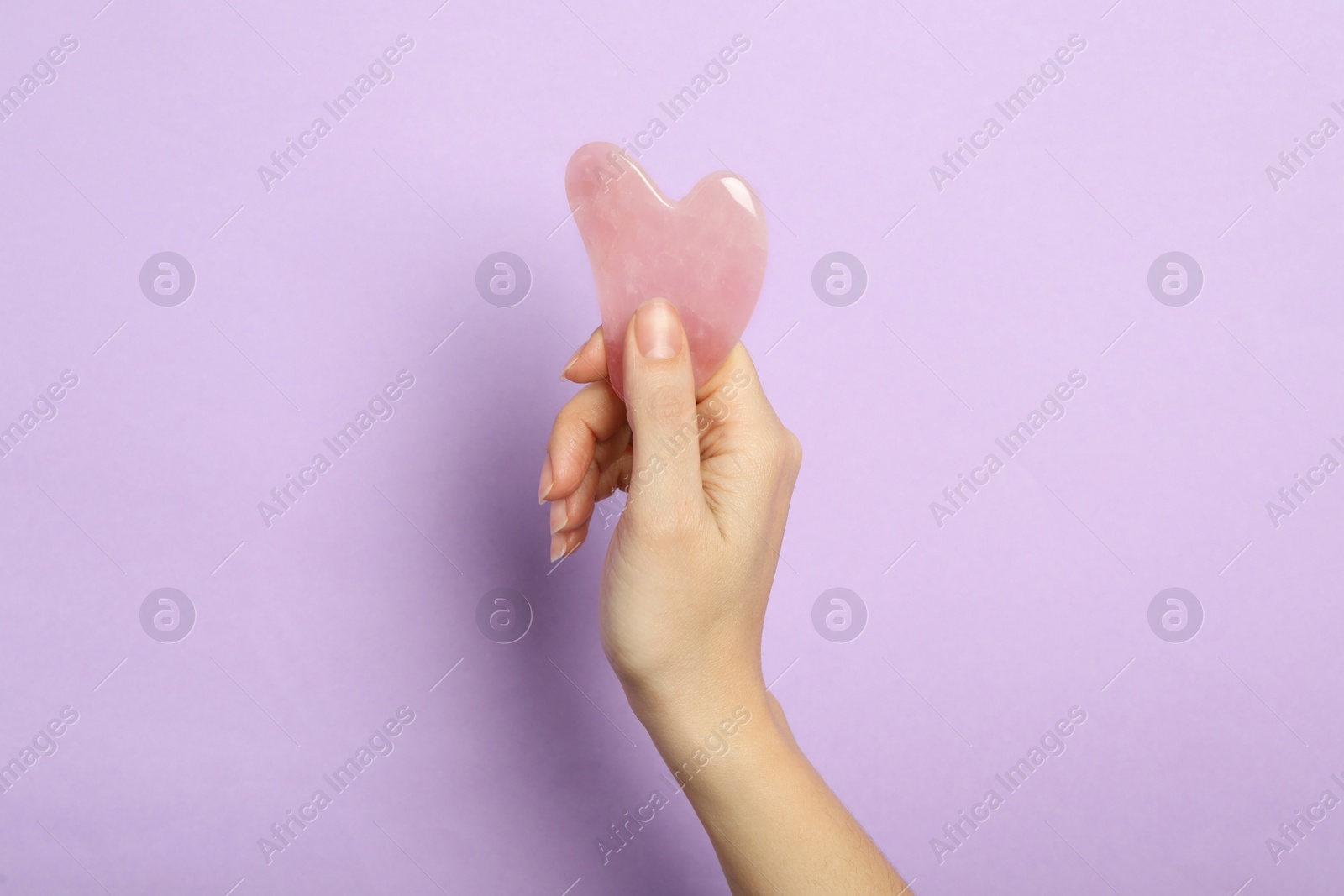 Photo of Woman with rose quartz gua sha tool on lilac background, closeup