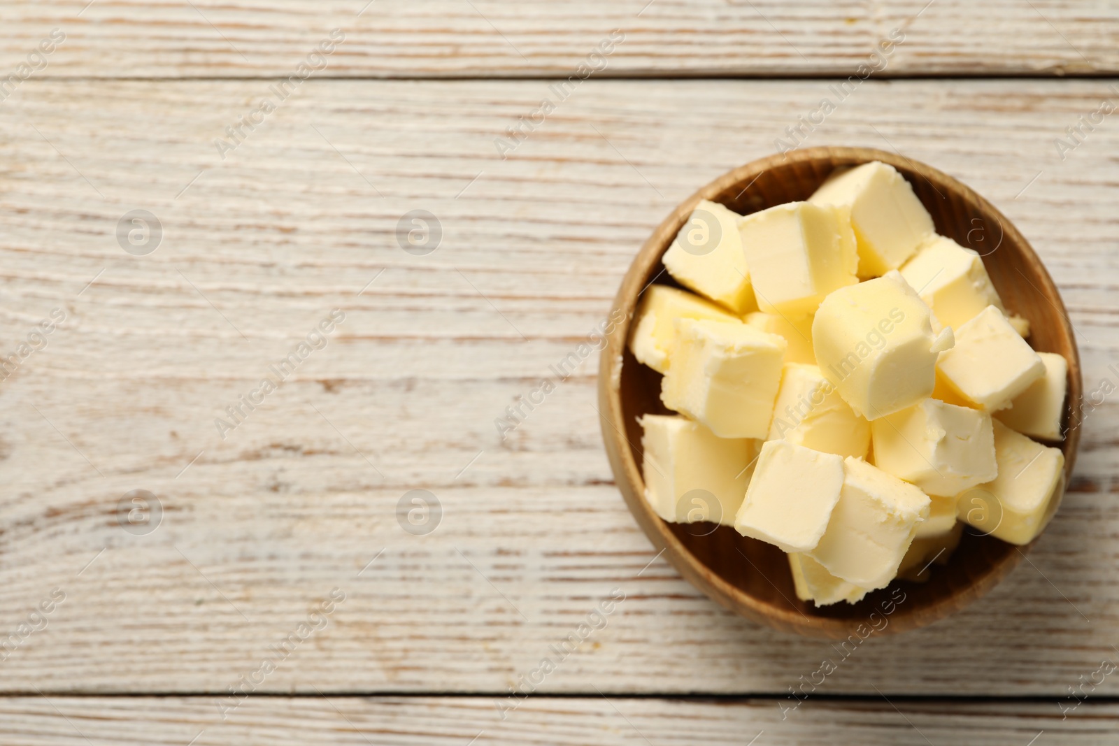 Photo of Tasty butter cubes in bowl on light wooden table, top view. Space for text