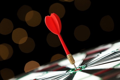 Red arrow hitting target on dart board against blurred lights