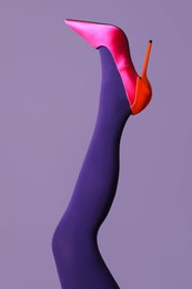 Photo of Woman wearing bright tights and high heel shoe on violet background, closeup