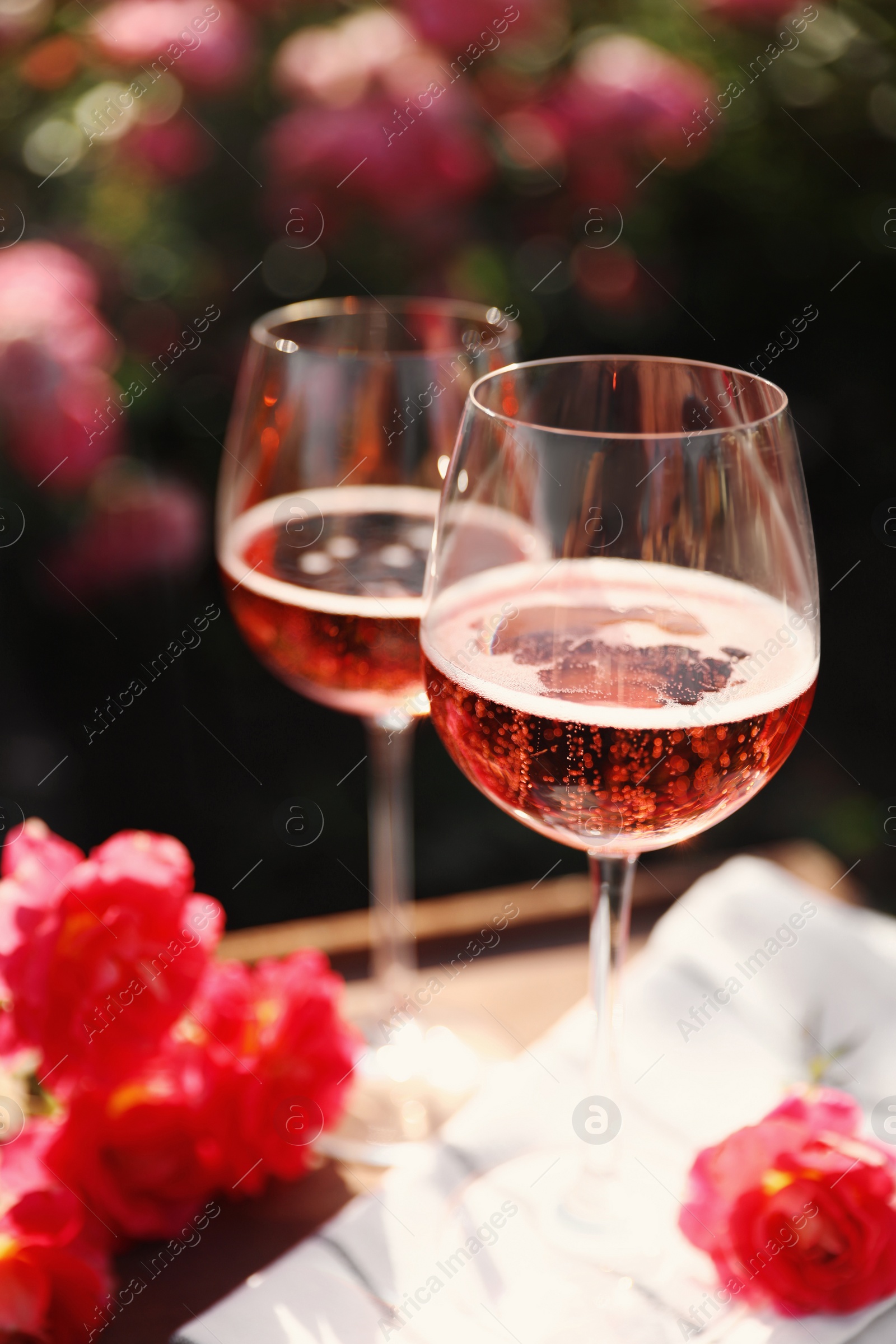 Photo of Glasses of rose wine on table in blooming garden