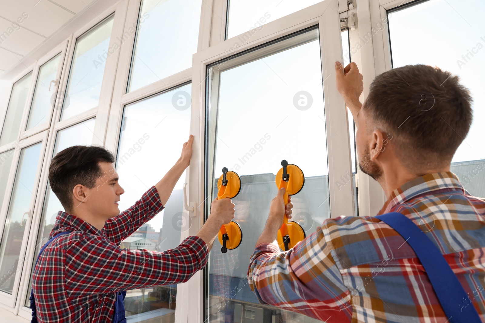 Photo of Workers using suction lifters during plastic window installation indoors