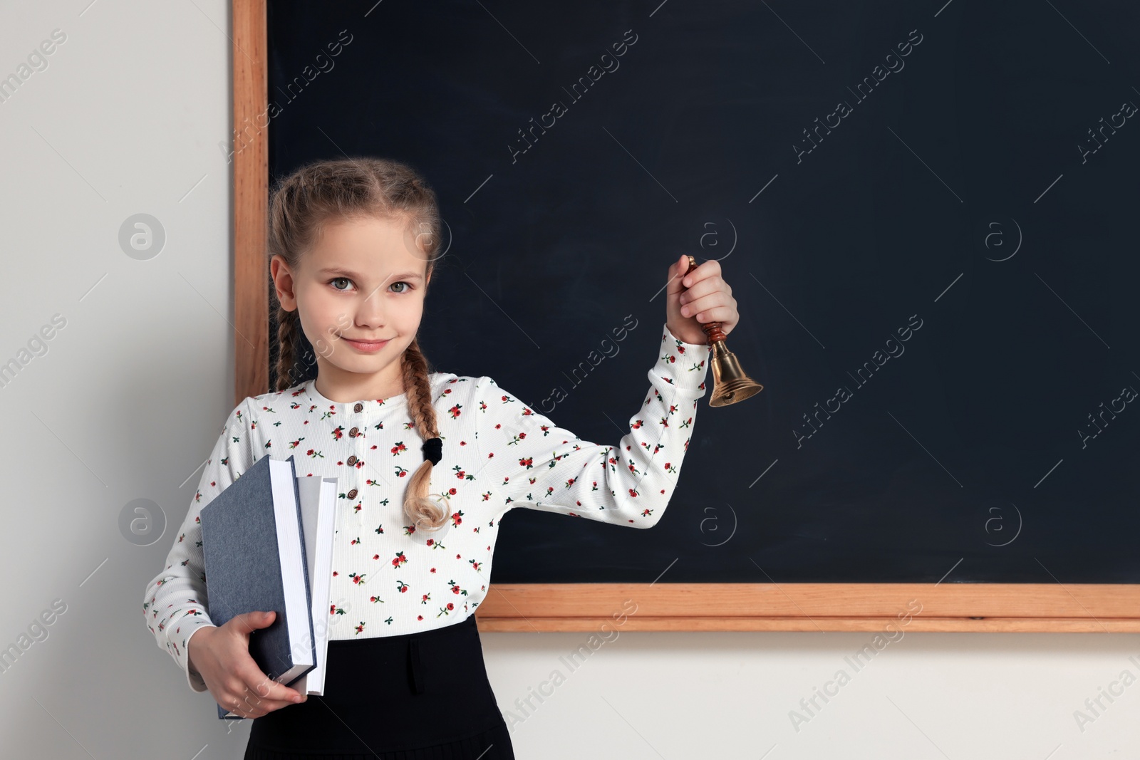 Photo of Pupil with school bell near chalkboard in classroom, space for text