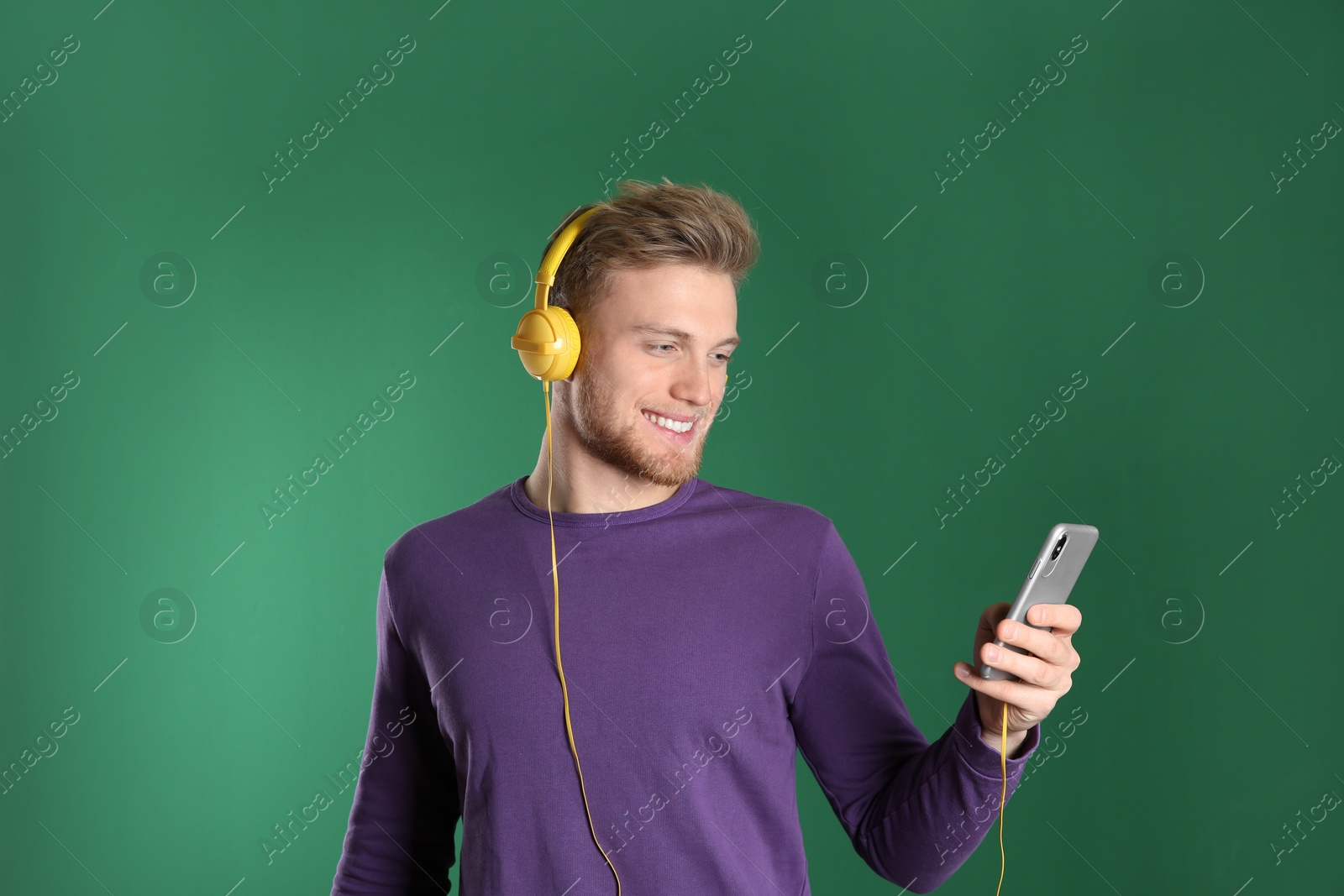 Photo of Handsome young man listening to music with headphones on color background