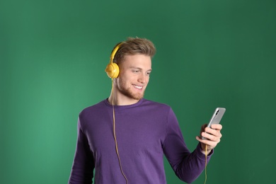 Handsome young man listening to music with headphones on color background