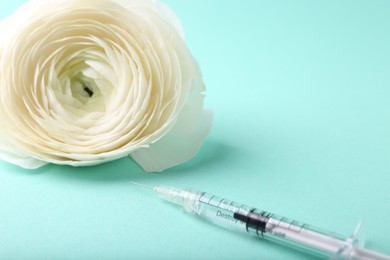 Cosmetology. Medical syringe and ranunculus flower on turquoise background, closeup