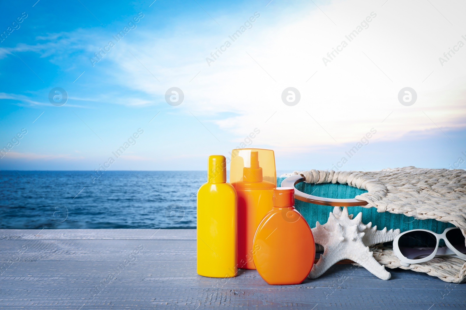 Image of Set of sun protection products and stylish accessories on wooden table near sea. Space for text